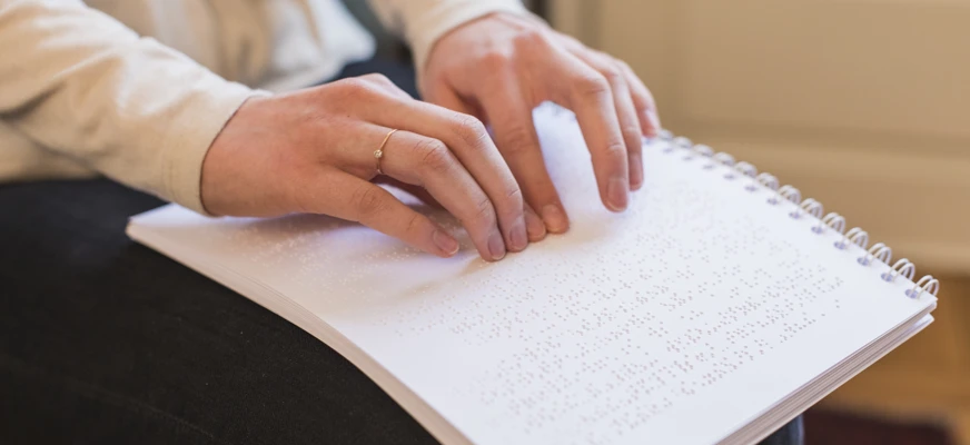 Händer läser punktskrift på ett papper.