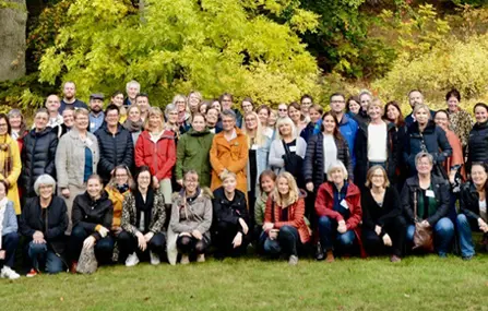 En stor grupp personer står samlade för fotografering utomhus i grönskan.