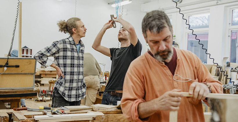 Tre vuxna män arbetar med trä i slöjdsal.