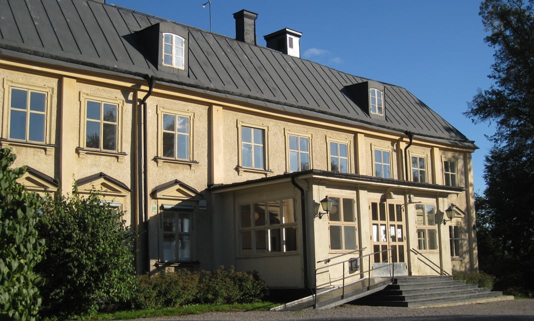 En gul herrgårdsbyggnad i solsken och blå himmel i bakgrunden.