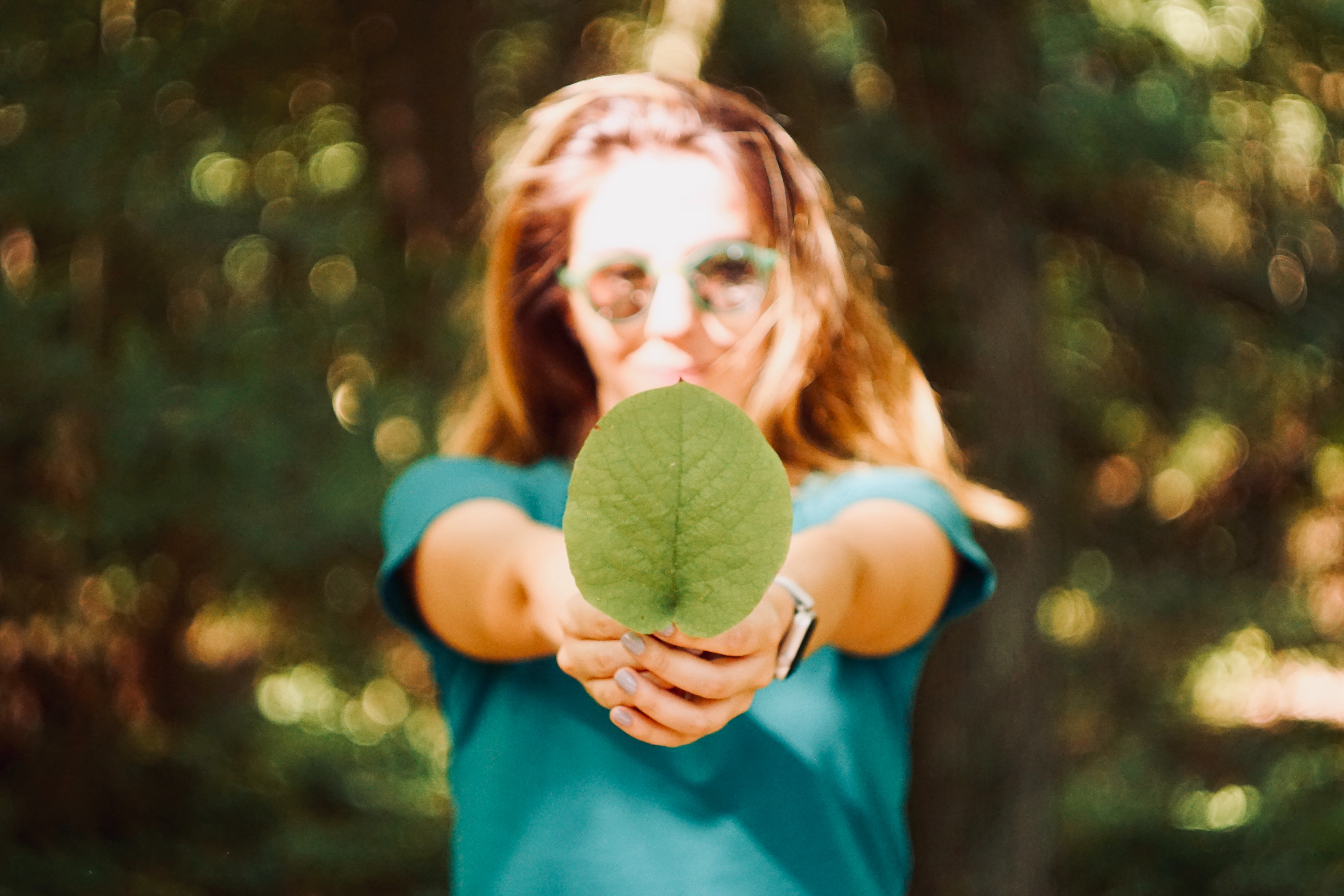 Kvinna i solglasögon håller i ett grönt löv, skärpa är på lövet.