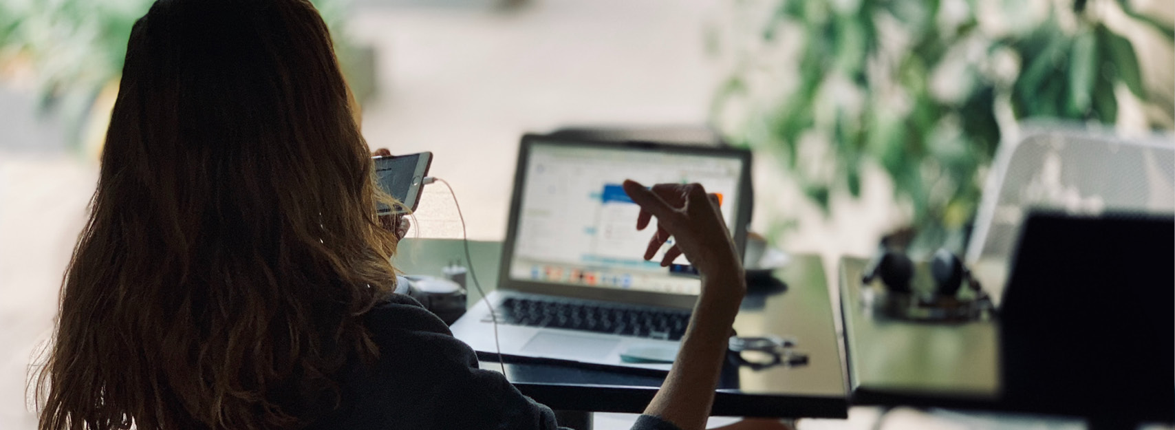 Person sitter framför datorskärm, håller i en telefon.