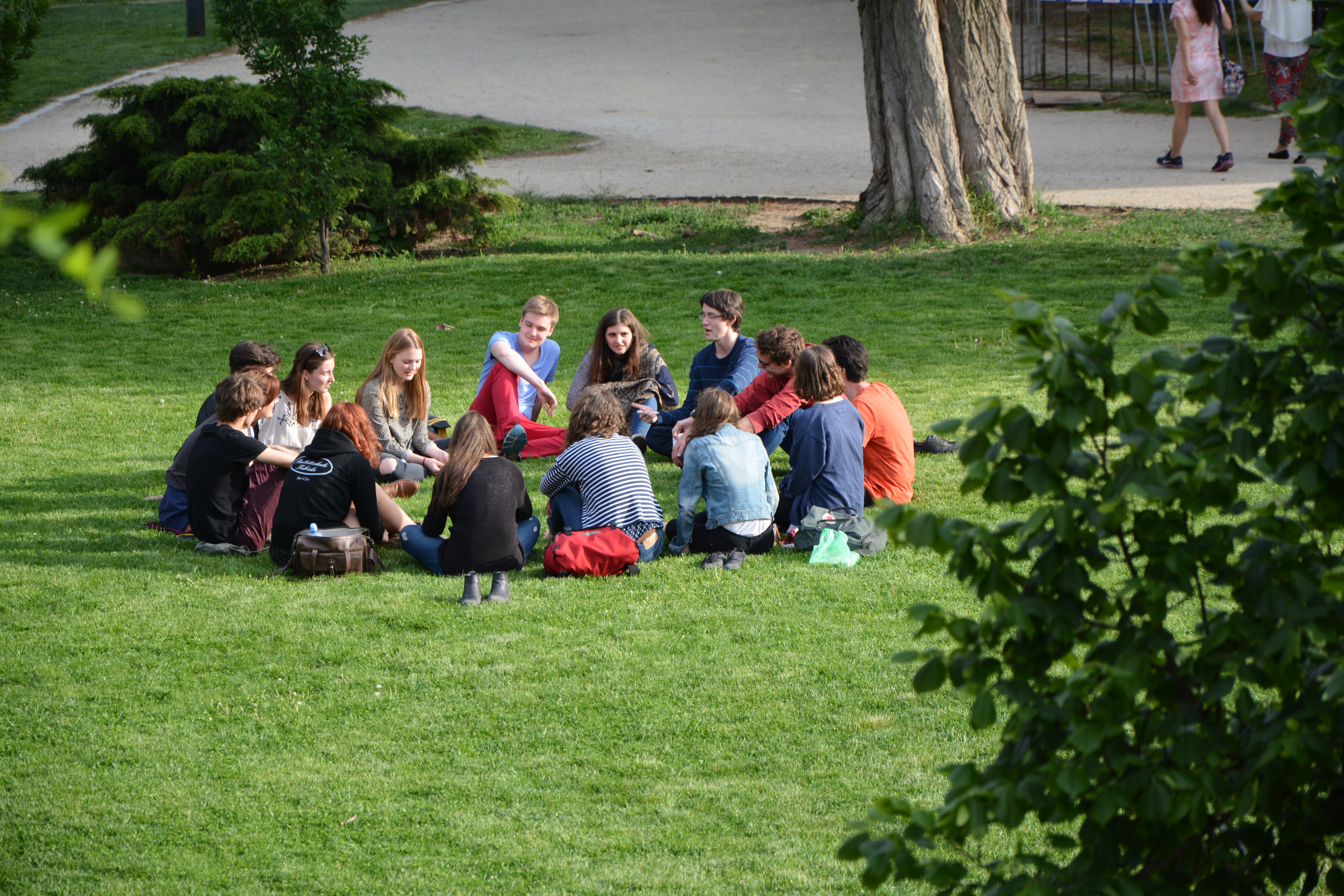 En grupp människor sitter i ring på en gräsmatta.