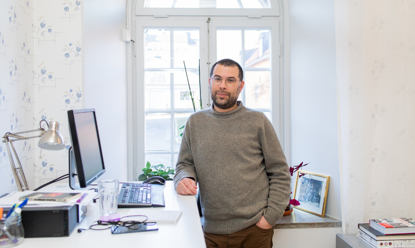 En person poserar vid ett skrivbord med en datorskärm. 